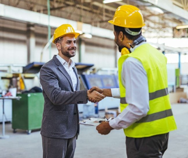 Workplace safety manager shaking hands with an industrial worker in a manufacturing facility.